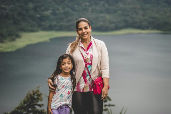A smiling mother and daughter embracing by a tranquil lake, exuding warmth and togetherness.