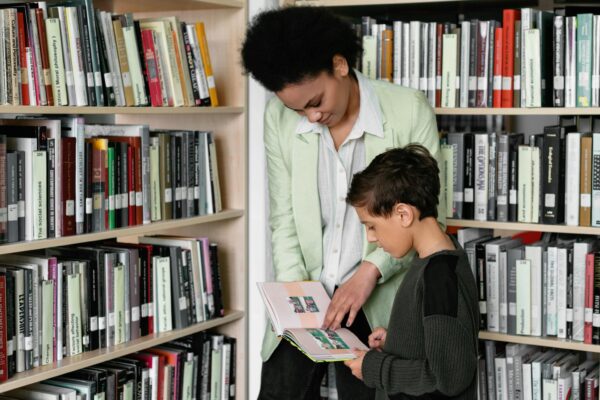 An adult helping a child read a book in a library setting, fostering learning.