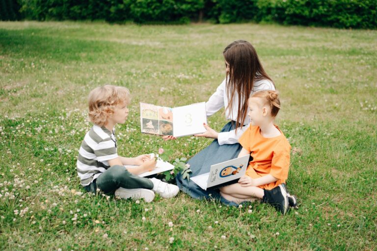 Two children and a woman enjoy a sunny outdoor reading session on the grass, enhancing their learning experience.